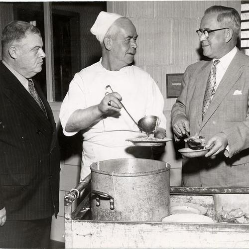 [Chef Stephen Clark showing County Jail Supt. Bill Hanley (left) and Sheriff Gallagher what he prepared as a luncheon meal for the inmates]