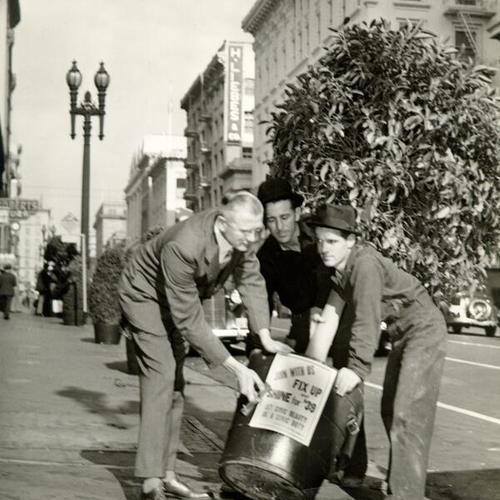 [Three men carrying a tree with planter with a sign attached to planter that reads 'Join With Us Fix Up Shine For '39']