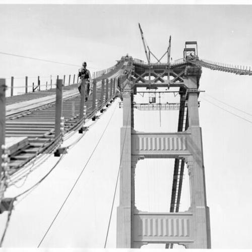 [Workman walking down the catwalk construction of Golden Gate Bridge]