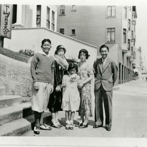 [Five people standing on sidewalk at Pine Street in 1934 with Buddhist church sign in background]
