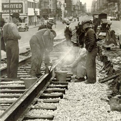 [Construction crews laying down tracks and ballast along Market Street]