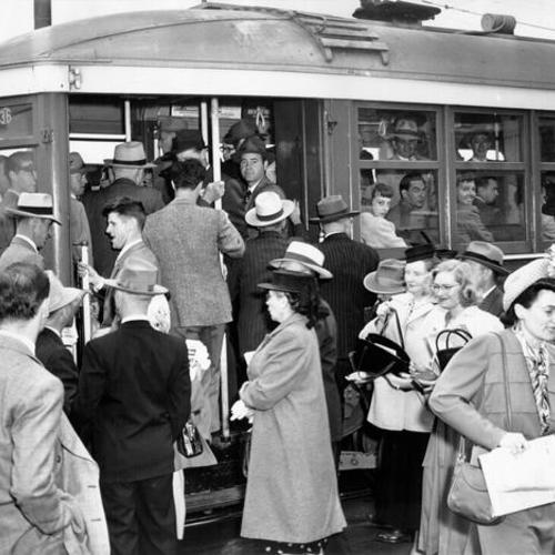 [People trying to board a crowded streetcar]