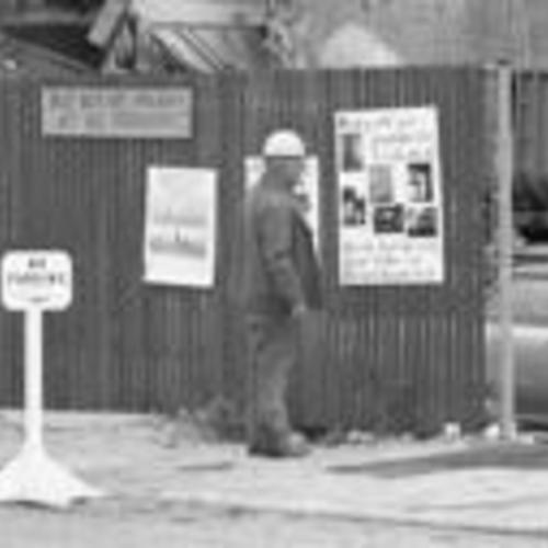 [Man in hardhat reads Tenants and Owners in Opposition to Redevelopment posters displayed adjacent to demolished building,
