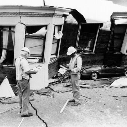 [Two Department of Public Works employees standing in front of a building destroyed in the October 17, 1989 Loma Prieta earthquake]