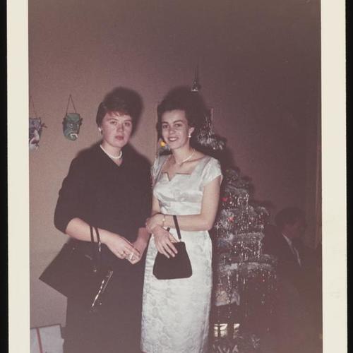 Two people standing in front of Christmas tree holding purses