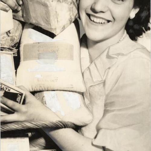 [Unidentified woman holding basket containing variety of food products]