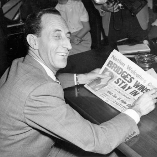 [Harry Bridges smiles as he reads newspaper headline cancelling an order calling for his deportation to Australia]