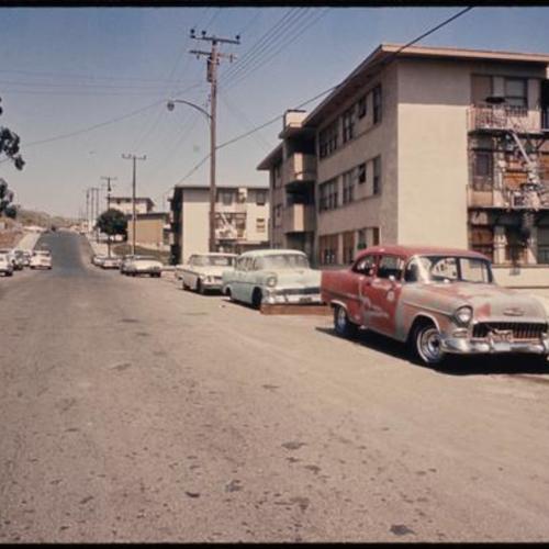Old cars parked along street with withered buildings and boarded up windows