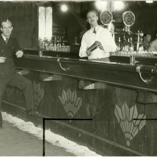 [Part owner Jerry Zucker, in white coat, and bartender Billie Sund posing with several other unidentified men at King Tut's bar located on the new Barbary Coast]