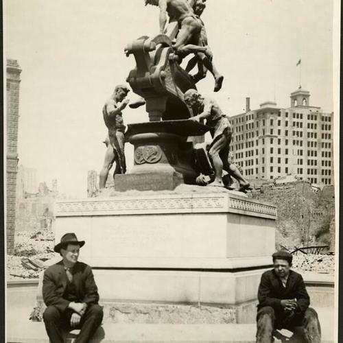 [Two people sitting at the base of the Donahue Monument, also known as the Mechanics Monument, at the intersection of Bush and Market streets]
