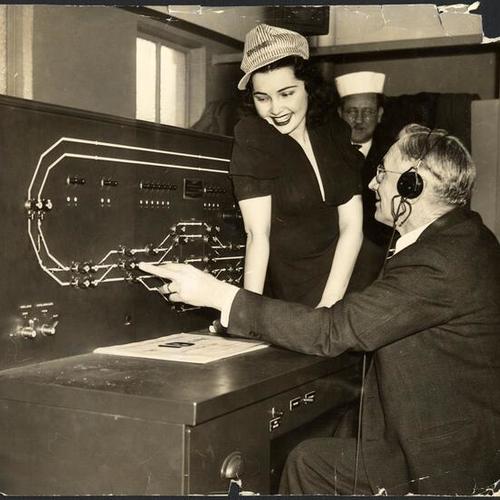 [Three unidentified people in a control room for the San Francisco-Oakland Bay Bridge electric railway system]