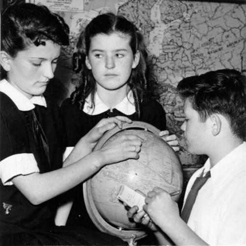 [Students Clotilde Perasso, Kathleen O'Conner and George Mitacek of Notre Dame des Victoires school tracing a shipping route on a globe]