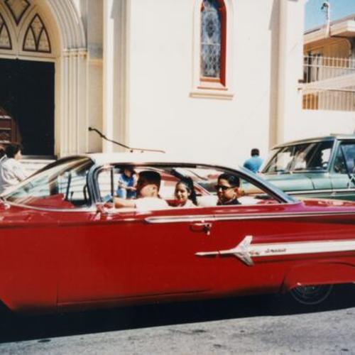 [Portrait of guests arriving in red Oldsmobile car for a Quinceañera at St. Peter's Church]