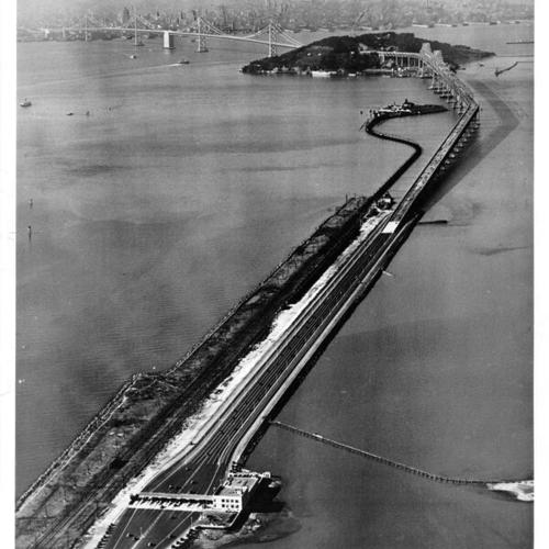 [Aerial view of Bay Bridge looking east showing toll booths, cantilever and suspension ends of bridge, Yerba Buena Island with San Francisco in background]