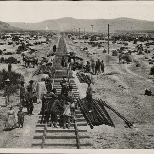 Workers laying rails in foreground followed by Chinese laborers in background that spaced and spiked them into the ties