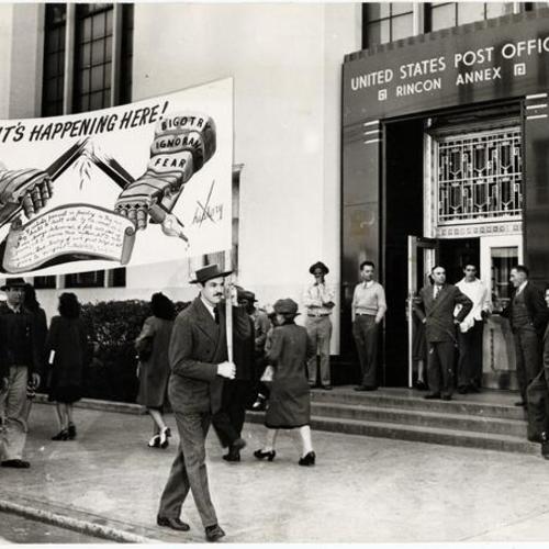 [Artist Anton Refregier and C.I.O. longshoremen union members carrying a banner in protest for the covering up of a section of a mural at the Rincon Annex Post Office]