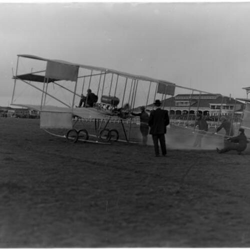 Louis Paulhan on biplane and crew at Tanforan racetrack stadium