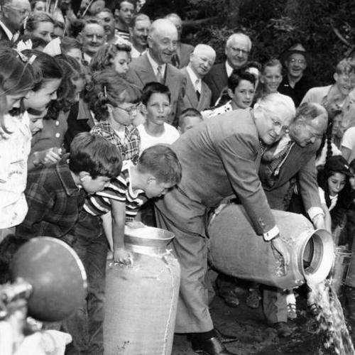 [Mayor Elmer Robinson and Chief Alan Taft, of the State Bureau of Fish Conservation, planting 500 bluegills in Middle Lake in Golden Gate Park as Park Commission members and children look on]