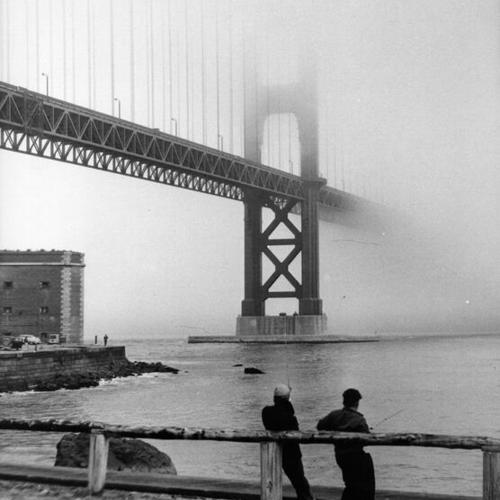 [Fog over Golden Gate Bridge and fishermen angling in foreground]