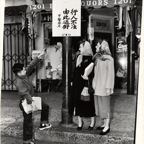 [Young man pointing to a traffic sign in Chinese, in front of 1201 Grant avenue, for two women]