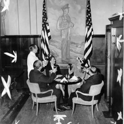 [Group of people drinking a toast to a portrait of General Douglas MacArthur at the Domino Club Cafe]