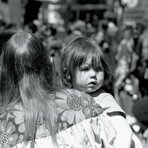 [Young child looks over mother's shoulder at summer festival]