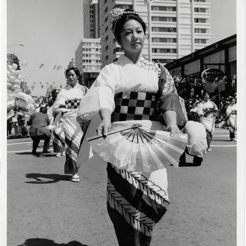 [Woman dressed in kimono with fan marches in Cherry Blossom Festival parade in Japantown]
