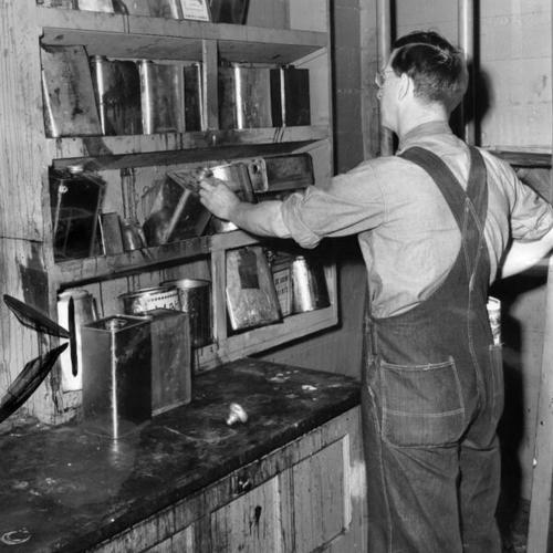 [Janitor James Connolly examining open wooden cabinet storing inflammable materials at Horace Mann Junior High School]