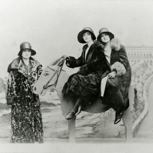 [Maria with two friends posing for a photo at a studio with photo background of Cliff House and Ocean Beach at Sutro Baths]