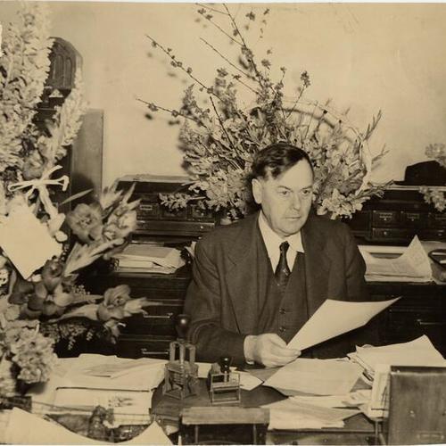 [Capt. Bernard J. McDonald at his desk surrounded by bouquets of flowers]