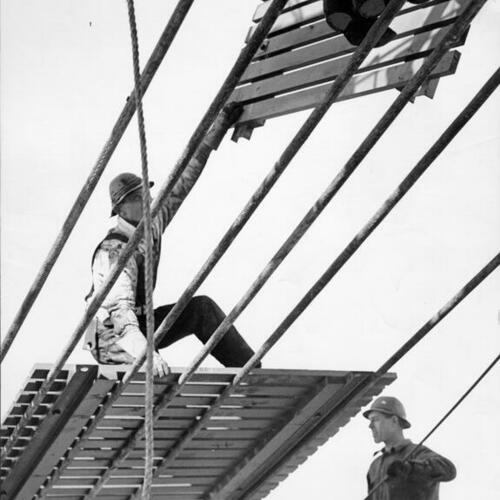 [Workmen laying catwalk construction of Golden Gate Bridge]