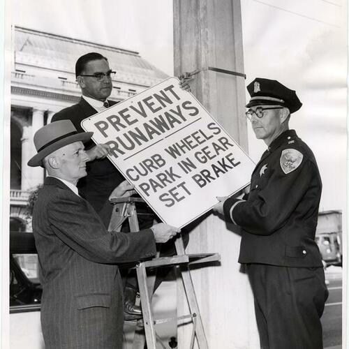 [(L to R) Director Harry A. Lee, Engineer Ross Shoaf, and Captain Ralph Olstad holding the first hillside parking sign]