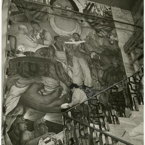 [Diego Rivera putting finishing touches on fresco decorating wall of Stock Exchange]