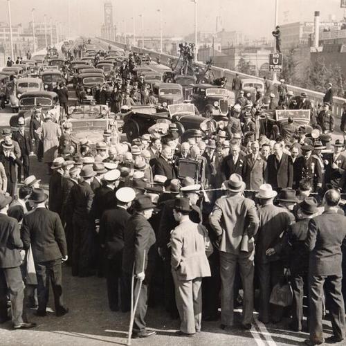 [Crowd consist of reporters, officials, polices, spectators, and vehicles gathering on bridge after an eight mile ride crossing the bridge in celebrating the opening of San Francisco-Oakland Bay Bridge]