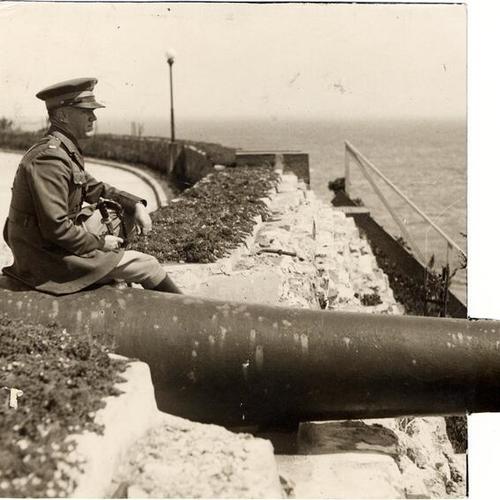 [U. S. Army soldier sitting next to large gun on Alcatraz Island]