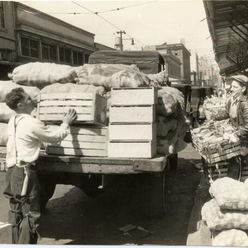 [Two workers unloading a produce truck in the Commission District]