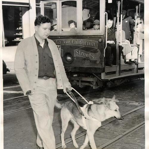 [J. D. Hayes crossing the street with his guide dog, Diane, at the intersection of California Street and Van Ness Avenue]