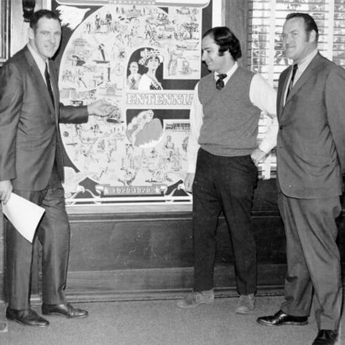 [Three unidentified people standing in front of a poster advertising the Golden Gate Park Centennial] 