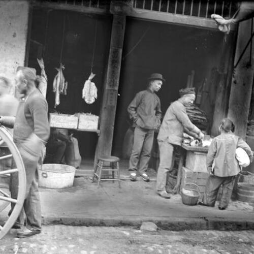 [Fish market; two men, child to right, three men to left, hanging dried fish]