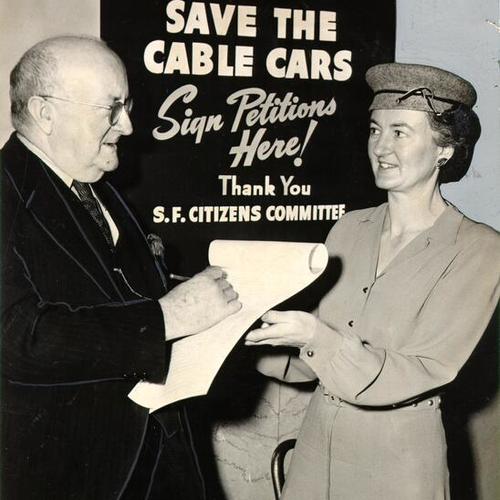 [John T. Johnson signing a petition, held by Mrs. Clark L. Mahany, to require the city to continue running its cable car lines]