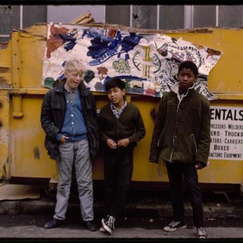 Three children standing in front of dumpster decorated with artwork