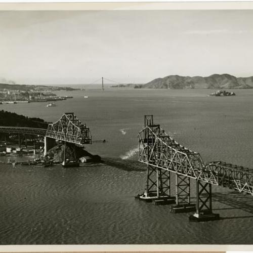 [Aerial view of construction of cantilever section of Bay Bridge with under construction Golden Gate Bridge in background]