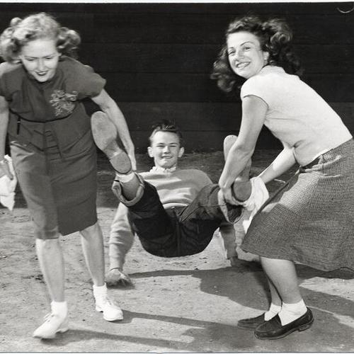 [Charlotte Huffman and Madge Lude dragging Jim Cosgrove by the legs during annual "Sadie Hawkins Day" race at San Francisco State College]