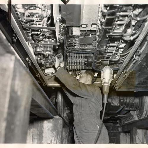 [Engineer Paul McSweeney fixing a wiring problem on a newly purchased Municipal Railway streetcar]