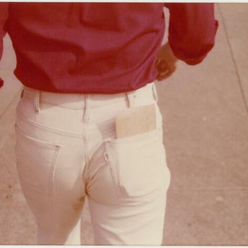 Backside of Bob Burkhart walking with envelope in back pocket
