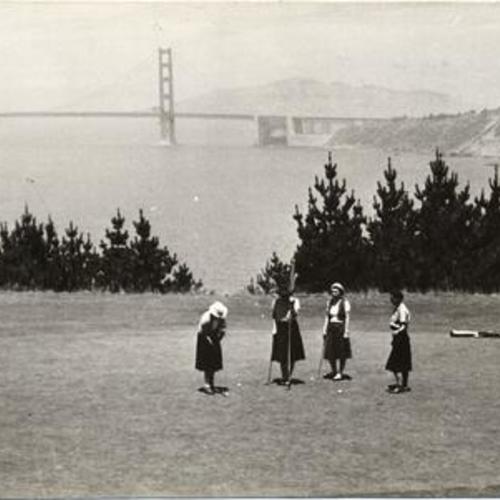 [Golfers playing on the 15th green at Lincoln Park Golf Course, with view of Golden Gate Bridge in background]