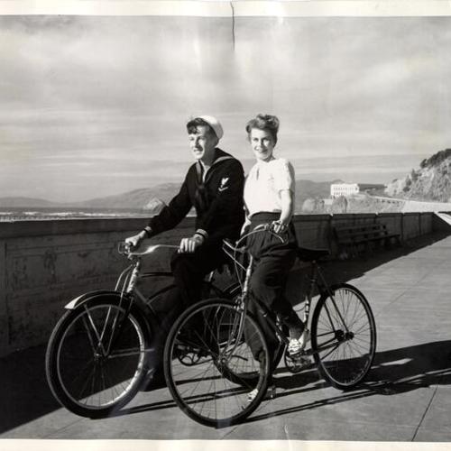 [Audrey Berman and a companion bicycling at Ocean Beach]