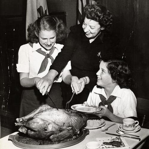 [Executive Director Catherine F. Stearns showing Camp Fire Girls Jackie Hauser and Anne Marie Gorman how to carve the turkey]