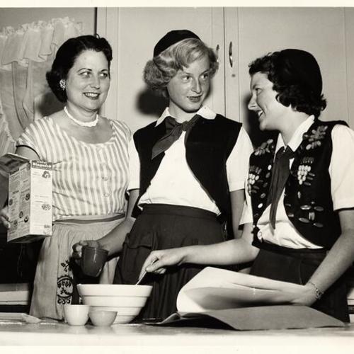 [Camp Fire leader Mrs. Richard Anthony oversees Judy Mayblum and Bonnie Burk food preparation abilities]
