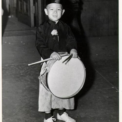 [Young boy dressed in costume holding a drum]